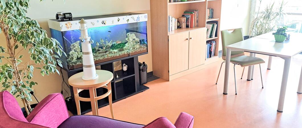 Die Bibliothek der Kurzzeitpflege „Friedensberg“  ist nebst Bücherregal, mit einer roten Couch und einem großen Aquarium gemütlich ausgestattet, Foto: Netzwerk für Menschen