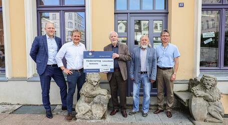 Wulf Kawan (M.), Ortskurator der Deutschen Stiftung Denkmalschutz, und Oberbürgermeister Rico Badenschier (2.v. l.) mit dem Förderbescheid zur Erhaltung der historischen Löwenbank vor der ehemaligen fürstlichen Apotheke, Foto: maxpress