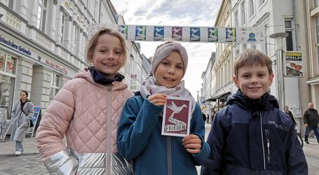 Paula Koball (Mitte) zeigt mit ihren Freunden Isabella (l.)und Adam (r.) auch die Postkarte mit dem Friedensmotiv