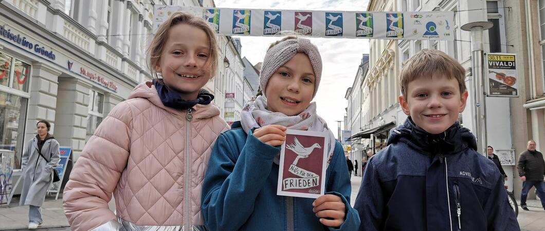 Paula Koball (Mitte) zeigt mit ihren Freunden Isabella (l.)und Adam (r.) auch die Postkarte mit dem Friedensmotiv